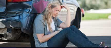 Woman with injuries sitting next to rear-ended car holding head in hands