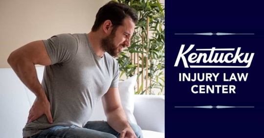 Man sitting on couch in pain holding lower back.